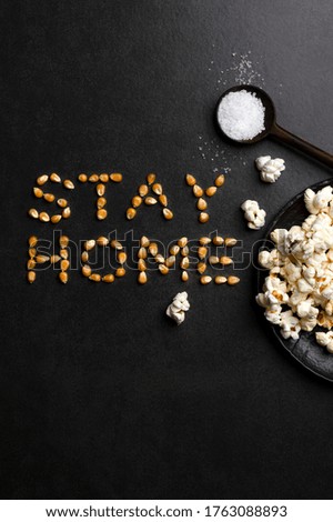 Stay home written by corn seeds letters food typography, salt and popcorn isolated on dark background. Home cooking and relax in quarantine, coronavirus, social distancing