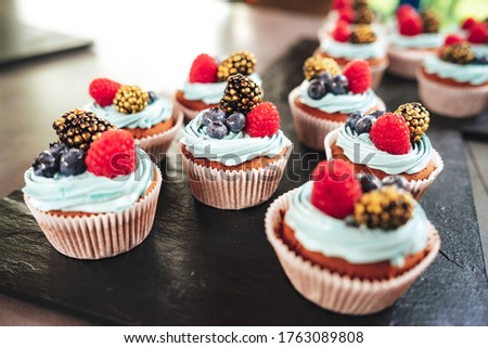 Sweet cupcakes with forest berries on black serving tray. Desserts at party. Celebration, party, birthday or wedding concept. Image