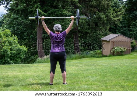 Middle aged caucasian woman with gray hair lifting a barbell with black plates, fitness outside on the lawn
 Royalty-Free Stock Photo #1763092613