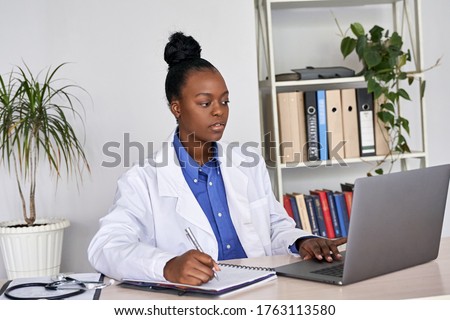 Serious african female doctor watching online medical webinar seminar training elearning on laptop make notes. Black woman physician gp participate video conference call videoconferencing on computer. Royalty-Free Stock Photo #1763113580