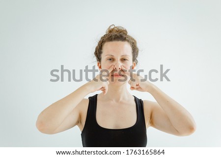 An attractive girl doing face fitness exercises, to prevent the appearance of wrinkles. The concept of non-surgical rejuvenation and self-care.