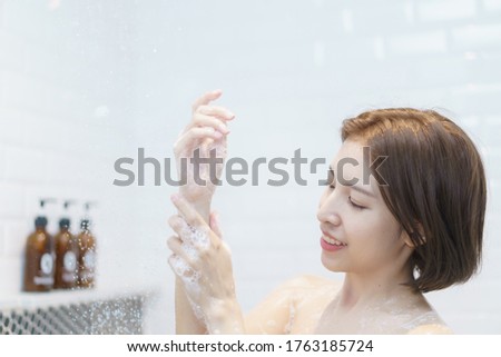 Woman taking a shower, washing her hair in a bathroom.