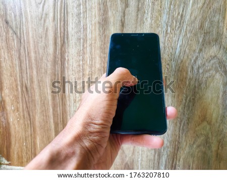 a one-handed portrait of a man holding a smartphone against an old wooden wall
