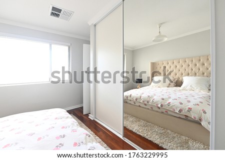 Empty home bedroom with double bed reflecting from a built-in wardrobe mirror.