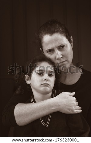 Upset mother and daughter sitting in the dark looking at camera isolated on black background.