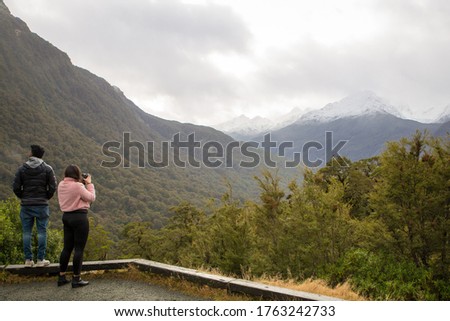 Two asian tourists take photos of the scenery at a lookout on Milford Road, Fiordland National Park, New Zealand