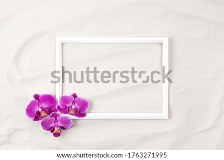 Top  view of white  photo frame on sand  background decorated with purple orchid flowers. Summer and vacation concept. Flat lay.  Copy space. 