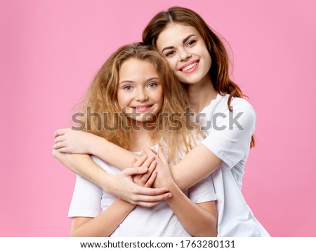Beautiful woman and little girl hugging on a pink background
