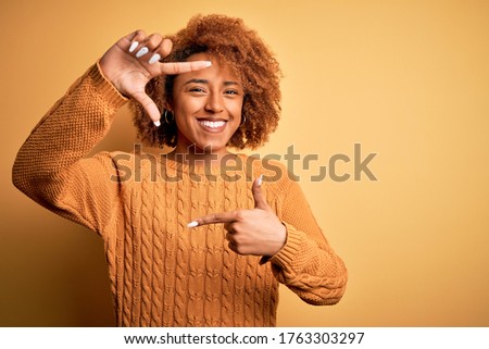 Young beautiful African American afro woman with curly hair wearing casual sweater smiling making frame with hands and fingers with happy face. Creativity and photography concept.