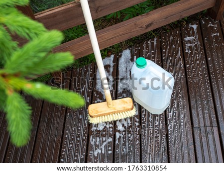 Brush and plastic canister with detergent on a wooden board, wooden terrace. Technologies and tools for cleaning surfaces. Royalty-Free Stock Photo #1763310854