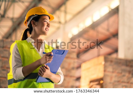portrait of smart asian female engineer inspector hand hold paper chart inventory checking smile confident with background of ware house and wooden pallet of product stock