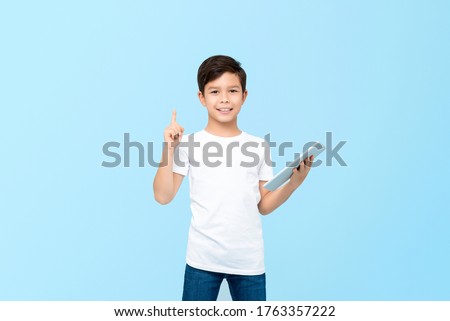 Cute 10 year-old mixed race boy holding tablet computer with one hand pointing to empty space upward isolated on light blue background Royalty-Free Stock Photo #1763357222