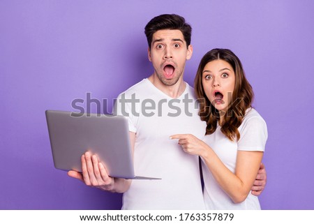 Look unbelievable. Astonished two people spouses hug hold laptop indicate corona virus epidemic information point index finger stare stupor wear white t-shirt isolated purple color background