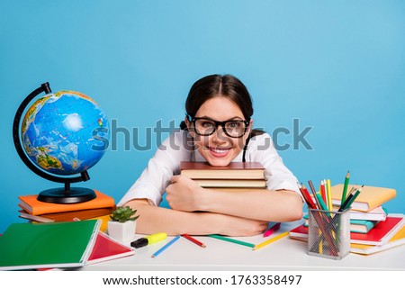Photo positive smart high school student sit table hug embrace pile stack textbook enjoy academic courses wear white black bouse overalls ponytails uniform isolated blue color background