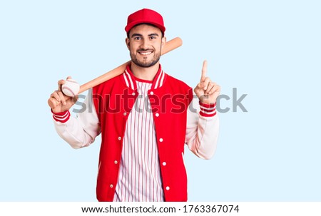 Young handsome man holding baseball bat and ball surprised with an idea or question pointing finger with happy face, number one 