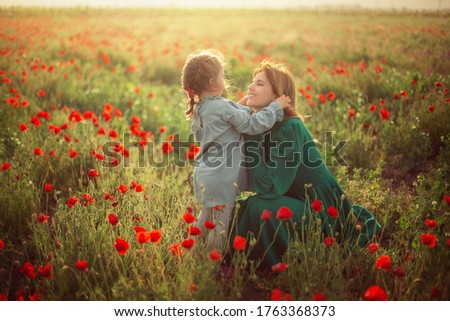 Mom with daughter in vintage dresses and hats play on the field with poppies in the rays of the setting sun