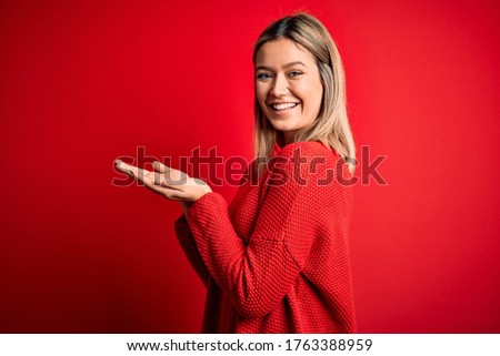 Young beautiful blonde woman wearing casual sweater over red isolated background pointing aside with hands open palms showing copy space, presenting advertisement smiling excited happy