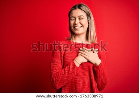 Young beautiful blonde woman wearing casual sweater over red isolated background smiling with hands on chest with closed eyes and grateful gesture on face. Health concept.