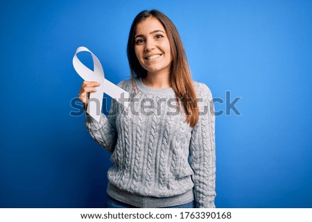 Young blonde woman holding cancer awareness and stop women violence white ribbon with a happy face standing and smiling with a confident smile showing teeth