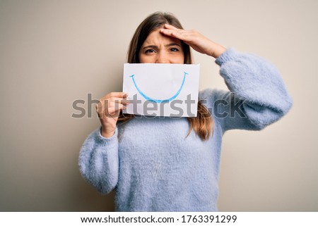 Young blonde woman holding funny smile drawing on mouth as happy expression stressed with hand on head, shocked with shame and surprise face, angry and frustrated. Fear and upset for mistake.