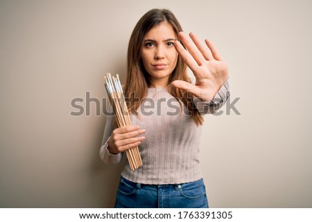 Young painter artist woman painting using paintbrush over isolated background with open hand doing stop sign with serious and confident expression, defense gesture