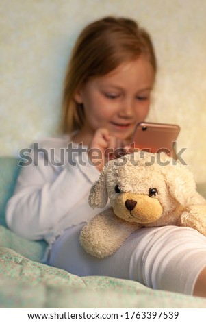 Child studying distance learning.Curious cute preschool girl using phone app looking at cellphone device sitting on couch alone at home. Little smart kid holding smartphone,playing online mobile game.