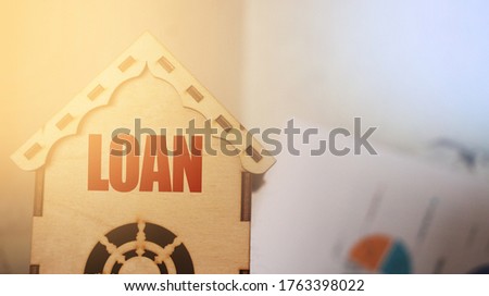 LOAN word on a small wooden toy house. Real estate loan social program or business project concept.