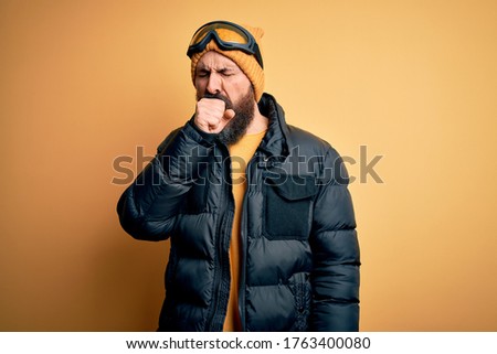 Handsome skier bald man with beard skiing wearing snow sportswear and ski goggles feeling unwell and coughing as symptom for cold or bronchitis. Health care concept.