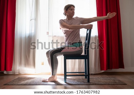 Woman working out doing yoga or pilates exercise using chair. Ardha Matsyendrasana pose variation. Royalty-Free Stock Photo #1763407982