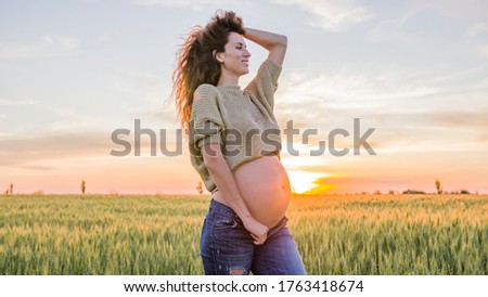 Beautiful Pregnant woman caressing her belly. Woman touching her tummy. Happy Expectant mother at nature in sunset.