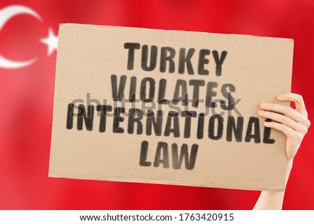 The phrase " Turkey violates international law " on a banner in men's hand with blurred Turkish flag on the background. Political negotiations. Relationship. Illegal actions. Legislation. Conflict
