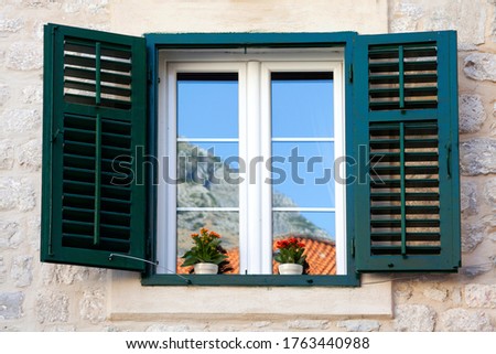 a typical window with louvered shutters and square paned windows with flowers in hanging flower pots Royalty-Free Stock Photo #1763440988