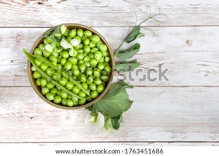 Top view Fresh raw green peas (Pisum sativum) in a wooden bowl with leaves and flower on a wooden table Royalty-Free Stock Photo #1763451686