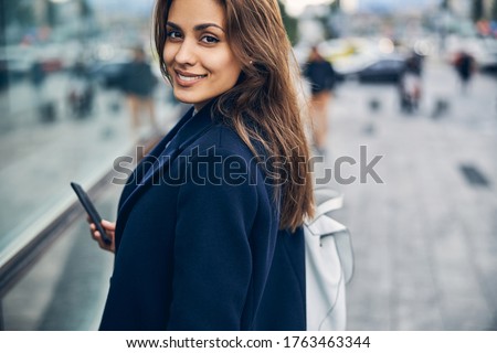 Portrait of attractive young woman with mobile in casual clothes smiling while looking into camera Royalty-Free Stock Photo #1763463344