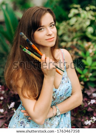 Portrait of a young artist in a blue dress with brushes in her hands. Botanical Garden.