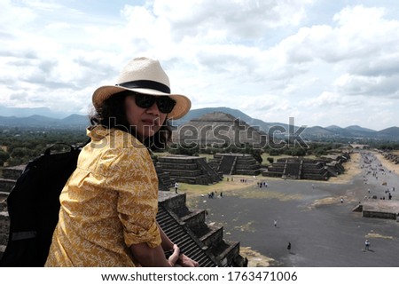 An Asian female tourist posing for a picture from the Pyramid of the Moon overlooking the Avenue of the Dead and Pyramid of the sun in the background in Teotihuacán Municipality.