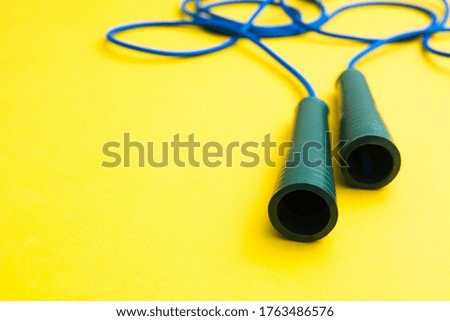 Blue fitness skipping rope for jumping with plastic handles on yellow background