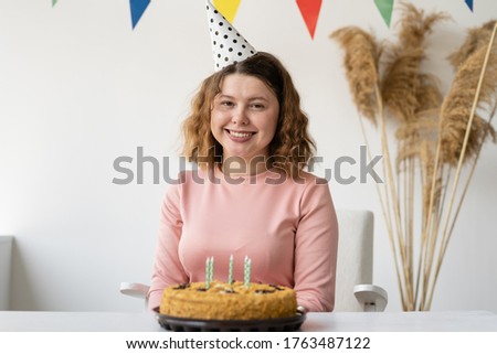 Beautiful young lady celebrates a birthday. She stands in the room and holds a cake in her hands. The house has a festive atmosphere and the beginning of a party for the birthday girl.