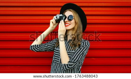 Portrait young woman photographer with vintage film camera over red wall background