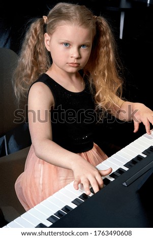 Vertical photo of young girl who is looking at the camera and playing the piano.