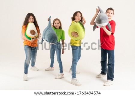 A group of children in bright clothes with their favorite soft toys in their hands on a white background. Studio photo. Baby modern trend soft toy avocado and shark