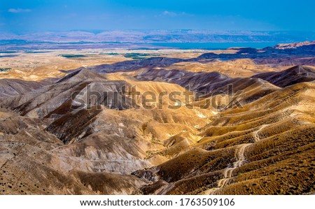 Brown hills of Judean Desert overlooking the Jordan Valley and the Dead Sea; Jordanean Mountains and towns in the distance Royalty-Free Stock Photo #1763509106