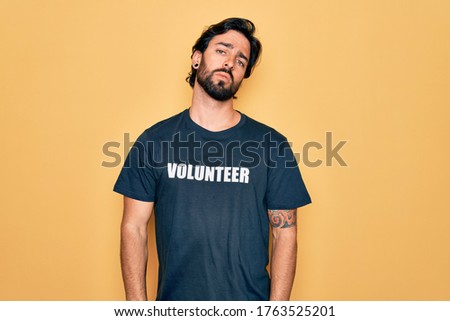 Young handsome hispanic volunteer man wearing volunteering t-shirt as social care looking sleepy and tired, exhausted for fatigue and hangover, lazy eyes in the morning.