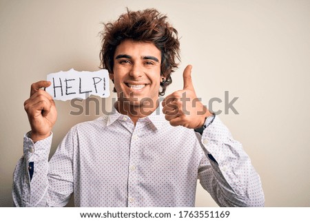 Young handsome man holding paper with help message over isolated white background happy with big smile doing ok sign, thumb up with fingers, excellent sign