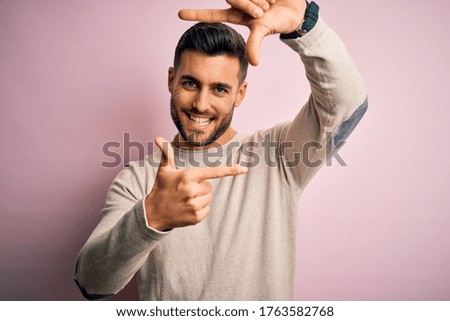 Young handsome man wearing casual sweater standing over isolated pink background smiling making frame with hands and fingers with happy face. Creativity and photography concept.