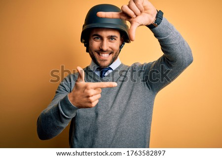 Young handsome businessman wearing military helmet over isolated yellow background smiling making frame with hands and fingers with happy face. Creativity and photography concept.