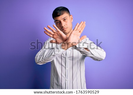 Young handsome hispanic man wearing elegant business shirt standing over purple background Rejection expression crossing arms doing negative sign, angry face