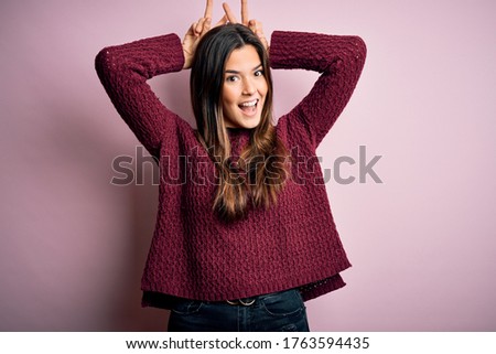 Young beautiful girl wearing casual sweater over isolated pink background Posing funny and crazy with fingers on head as bunny ears, smiling cheerful