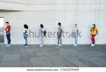 Multiracial people standing in a queue and waiting - Young people with social distancing and wearing protective face masks - Concept of the new normality and social distancing Royalty-Free Stock Photo #1763599409