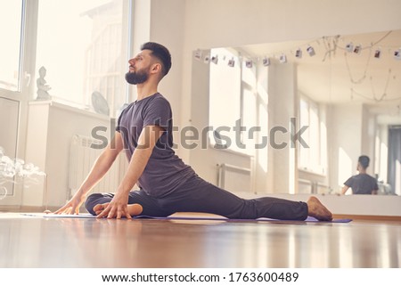 Bearded male in shirt sitting in pigeon position on the floor with incense stick
